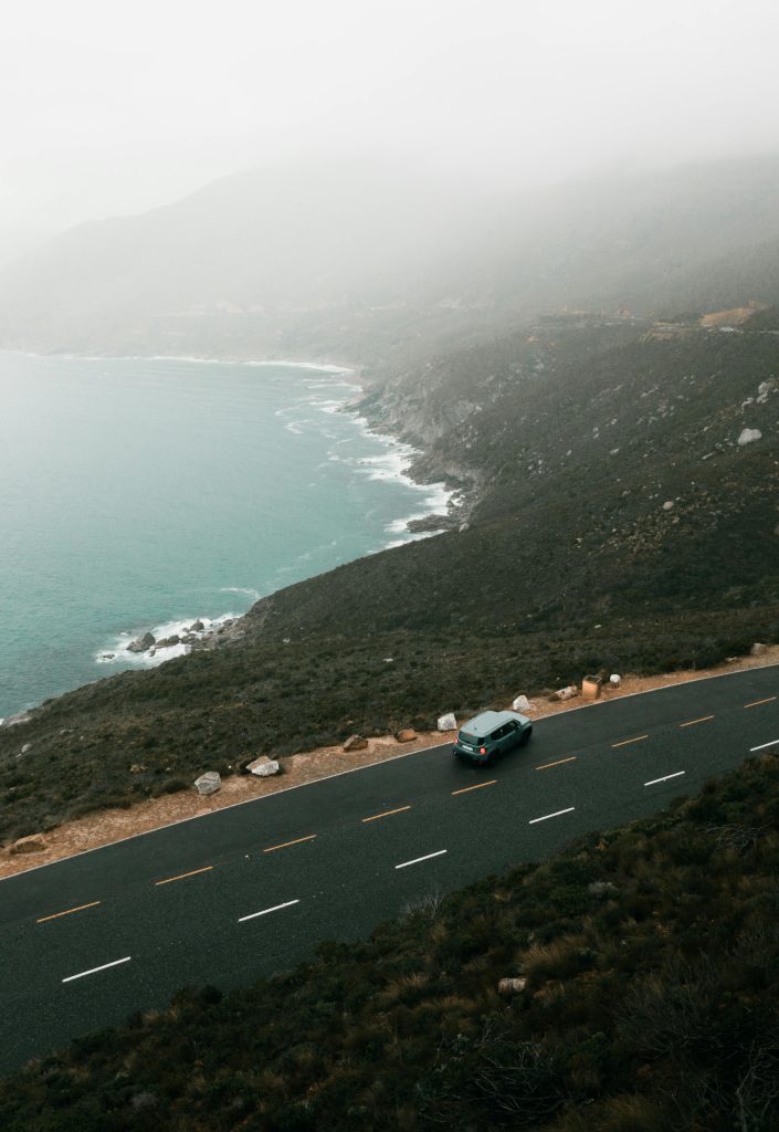A captivating aerial view of a solitary car driving on a coastal highway in Cape Town, South Africa.